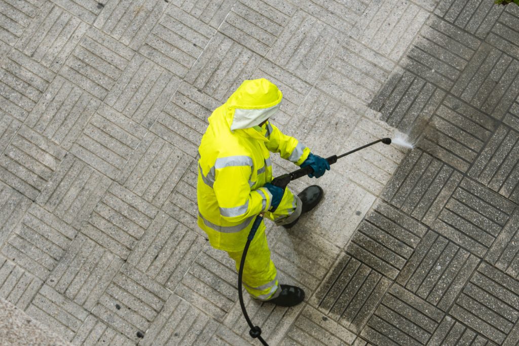 Top view of a Worker cleaning the street sidewalk with high pressure water jet on rainy day