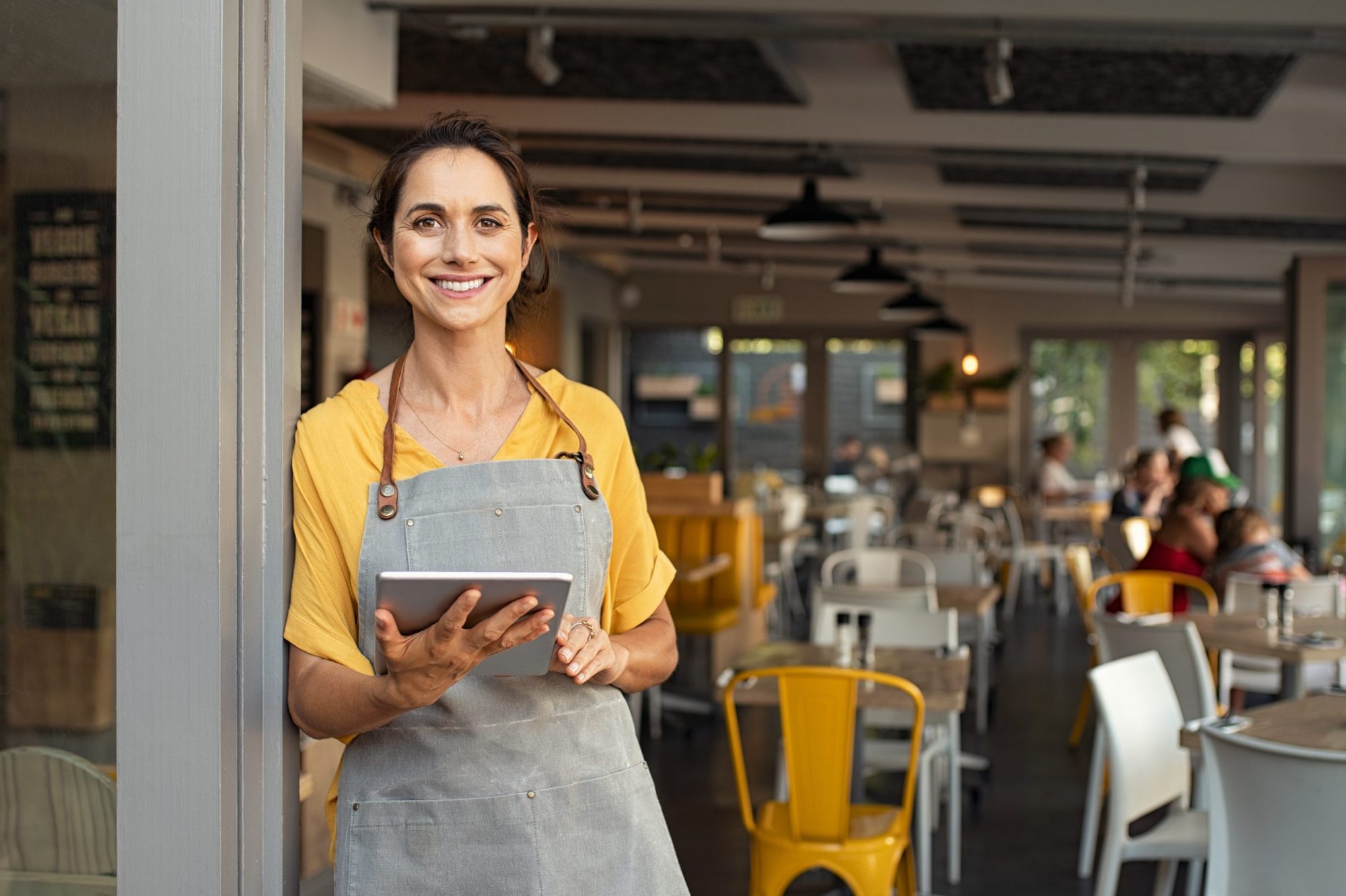 A female business owner standing right outside of her coffee shop with a tablet in her hands