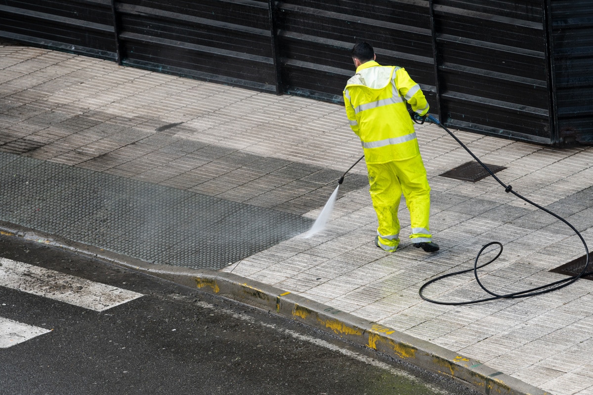 A man in a bright yellow outfit power washing the outside of a commercial property in El Paso.